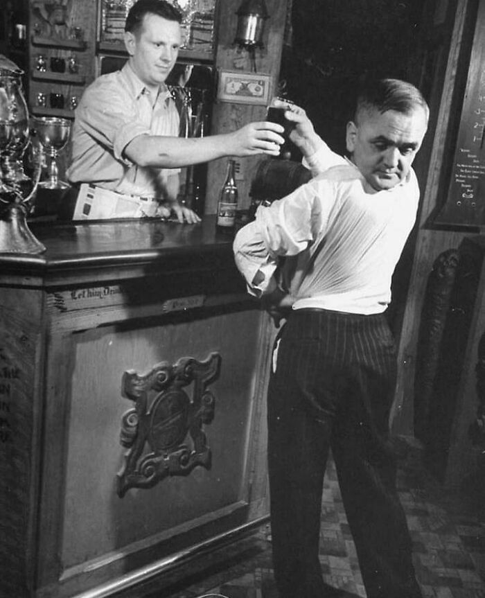 A truly bizarre old photo shows a bartender serving a drink to a man who appears to be reaching behind him.