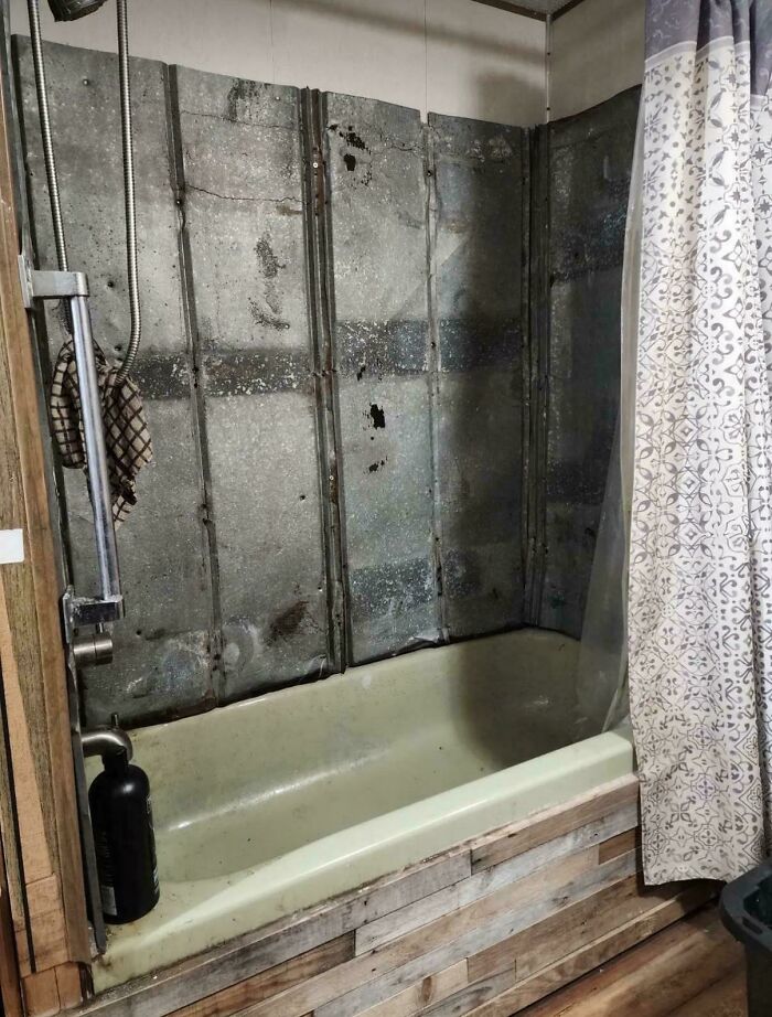 A bizarre shower with distressed metal walls and a shower curtain, a truly unusual bathroom setup.