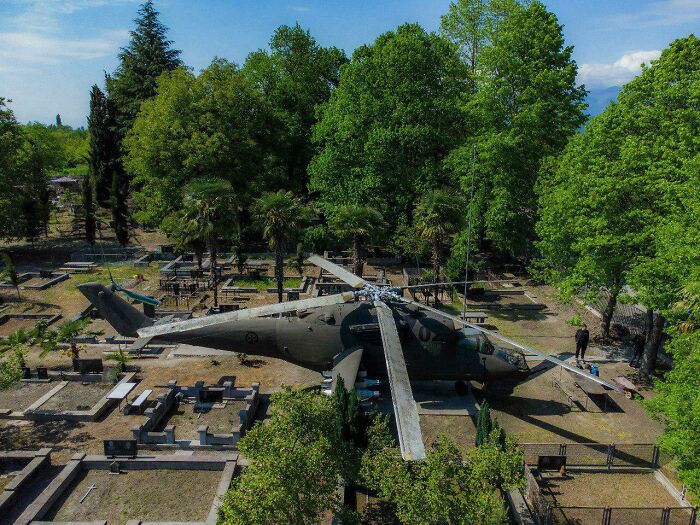 An old, bizarre helicopter in a cemetery, surrounded by trees and graves, a truly strange sight.
