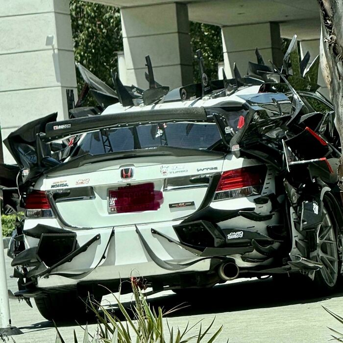 A white car heavily customized with many sharp, black, aerodynamic-looking attachments, a truly bizarre thing to take a photo of.