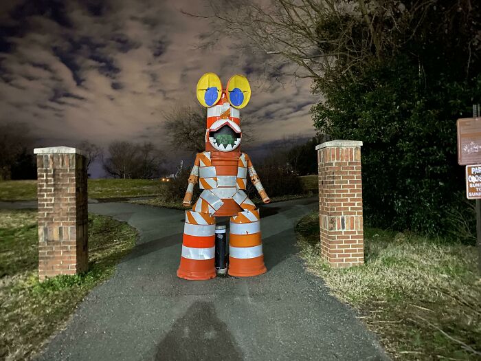 A bizarre thing: a creature made of traffic cones with large eyes and a toothy grin, standing on a path at night.