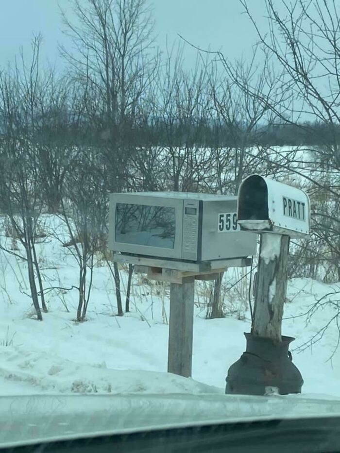 An unusual mailbox made from a microwave, a bizarre thing in a snowy, rural landscape.