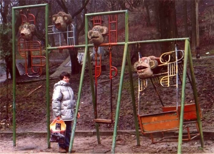 A person standing in front of an old, dilapidated playground with monkey-themed swings, a classic example of playground fails.