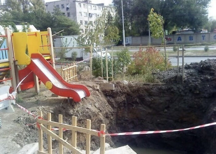 A red playground slide ending at the edge of a large, deep pit, showing a significant playground fail.