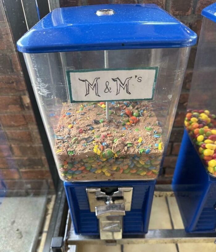 A candy dispenser filled with M&M's mixed with a lot of sand, a truly bizarre sight that makes you hallucinate.