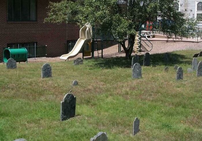 A playground with a slide and a green tunnel situated bizarrely close to a graveyard, showing playground fails.