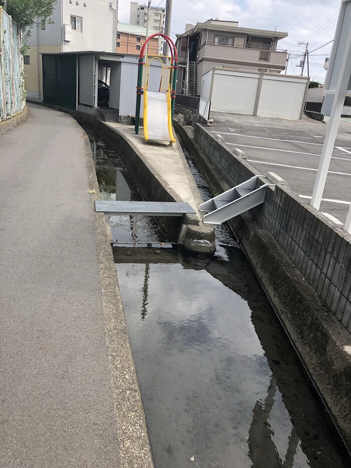 A playground slide leading directly into a narrow stream, showcasing a playground fail.