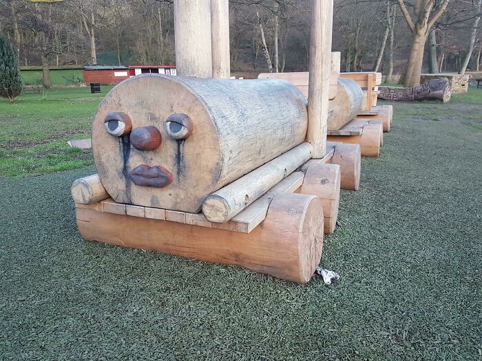 A wooden playground train with a sad, crying face, a unique and slightly unsettling playground fail.