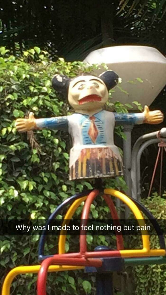 A distressed Mickey Mouse-like figure on a broken roundabout in a park, a severe playground fail.