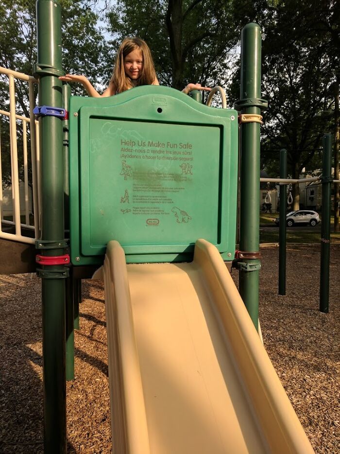 A young girl stands atop a playground slide, highlighting a potential playground fail in its design.