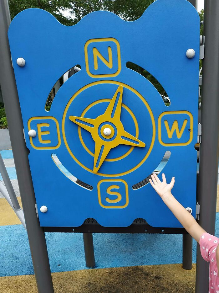 A child's hand reaching for a blue and yellow compass spinner on a playground, illustrating a playground fail.