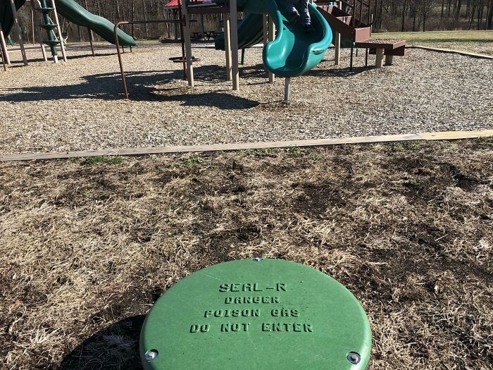 A green cap on the ground in a playground with a warning for danger and poison gas, highlighting a playground fail.