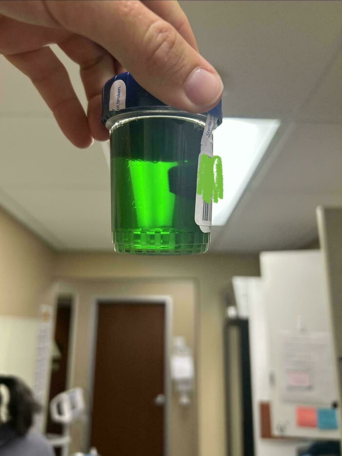 A hand holding a container of bright green liquid, a mildly interesting picture in a medical setting.