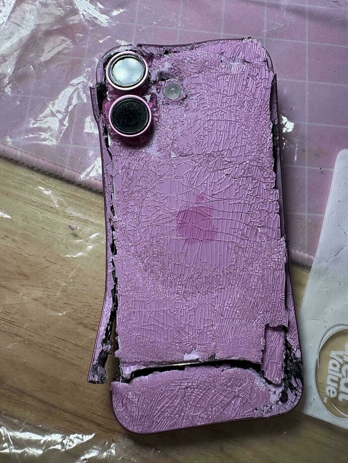 A severely cracked and damaged purple smartphone, showcasing a mildly interesting picture of its ruined back.