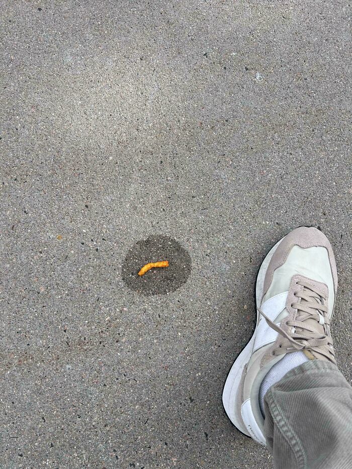 A pair of sneakers next to a mildly interesting picture of an orange snack on the sidewalk.