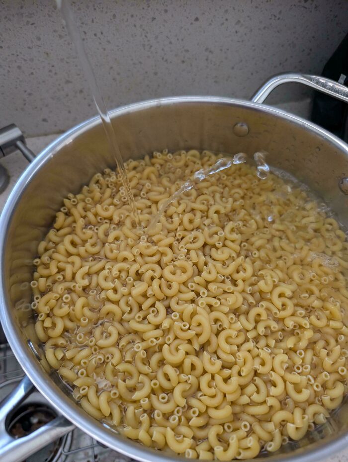 Mildly interesting picture of a pot filled with elbow macaroni, with water being poured over it.