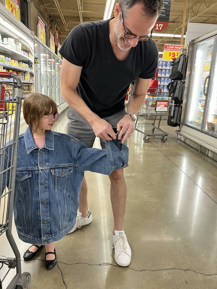 A man adjusting a large denim jacket on a small girl in a grocery store, proof of the right man.