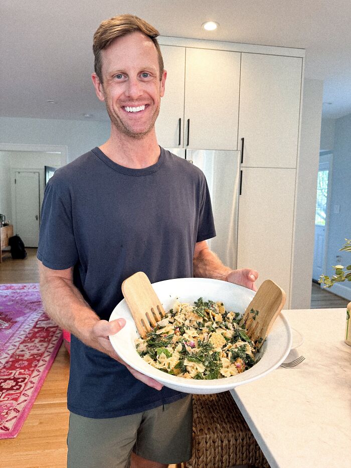 A man happily holding a large bowl of salad, a sweet proof he found the right man.
