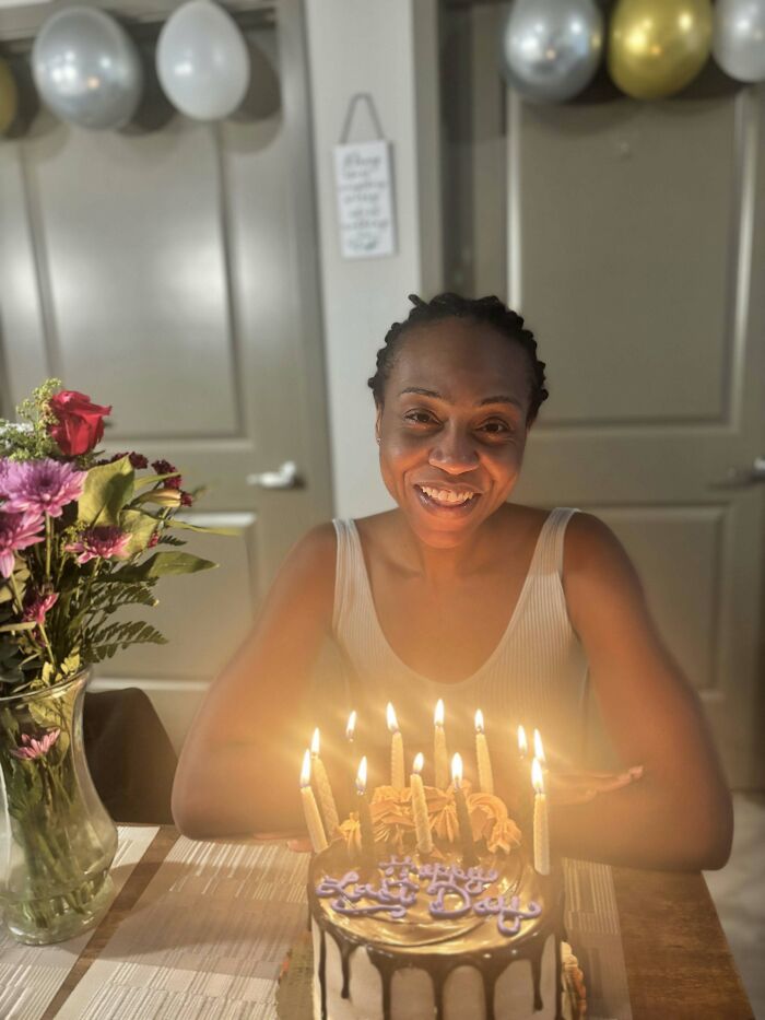 A smiling woman behind a lit birthday cake with flowers beside it. Proof of finding the right man.