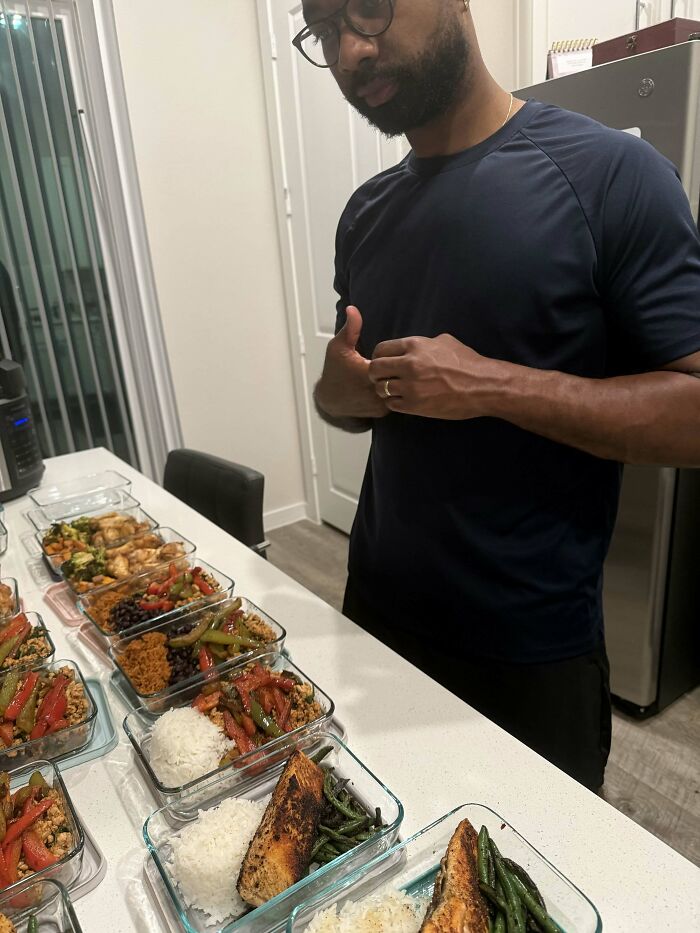 A man stands proudly behind a table filled with multiple meal prep containers. Proof of finding the right man.