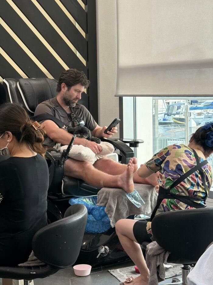 A man gets a pedicure while looking at his phone, a sweet proof of finding the right man.