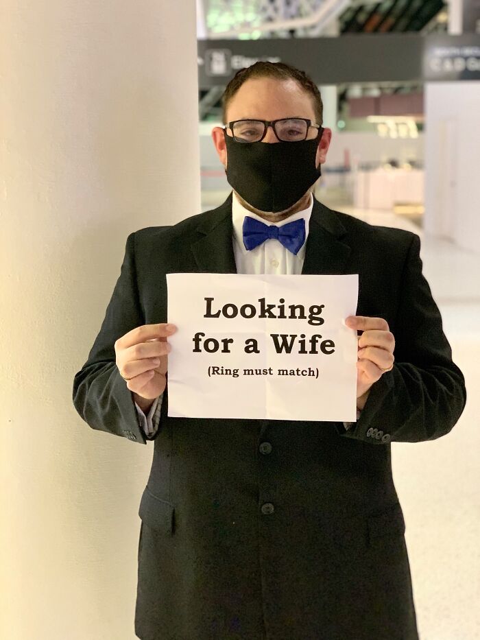 A man in a suit and a black face mask holding a sign looking for a wife. Proof of finding the right man.