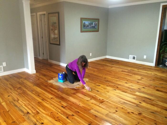 A woman on her knees, applying finish to a wooden floor as part of a home improvement project.