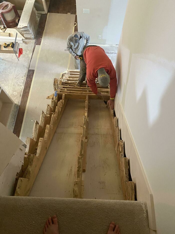 Two workers engaged in a questionable home improvement project, installing new stairs with an unusual frame visible.