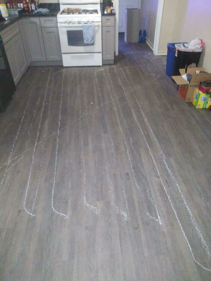 A kitchen with questionable home improvement project results, showing white chalk lines on the new grey laminate flooring.