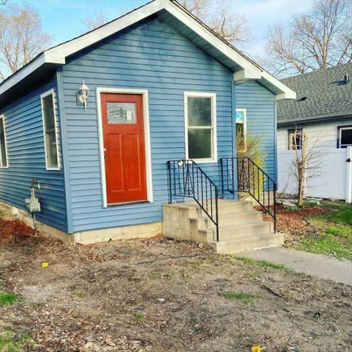 Questionable results from a home improvement project: a small blue house with a bright red door and poorly done landscaping.