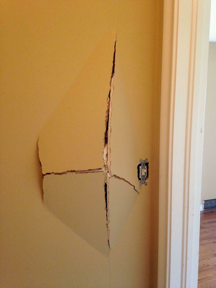 Questionable home improvement project: a large, deep crack in a yellow wall, exposing the drywall behind it.