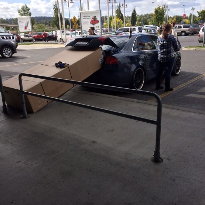 A large box protrudes from a car trunk, secured by a person, illustrating questionable home improvement transport.