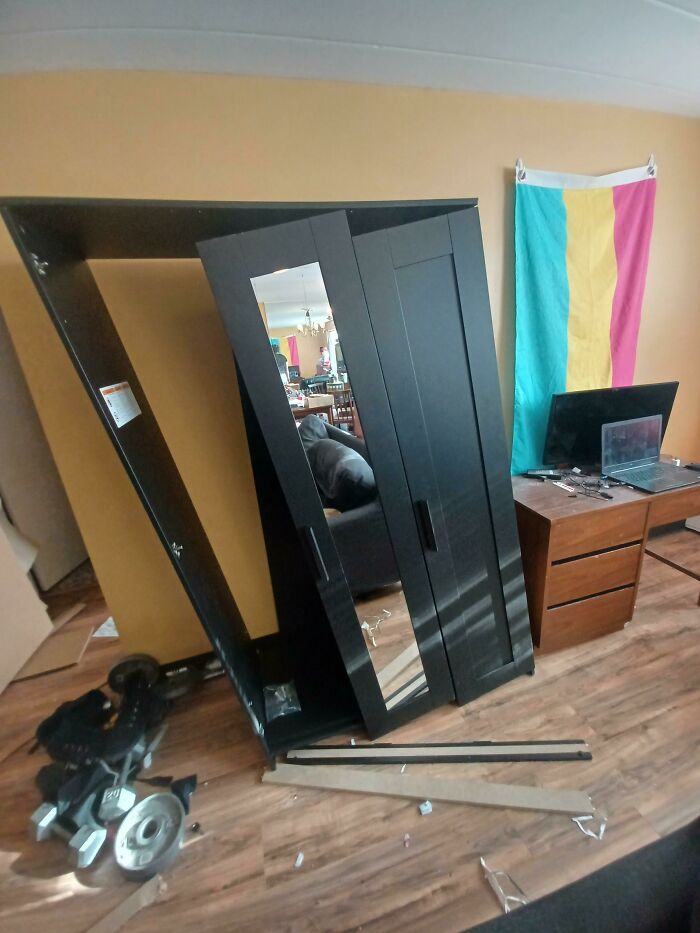 A black wardrobe has fallen over, obstructing a room, demonstrating questionable home improvement outcomes.