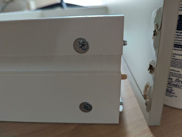 Close-up of poorly aligned screws and damaged wood on a furniture piece, demonstrating questionable home improvement.