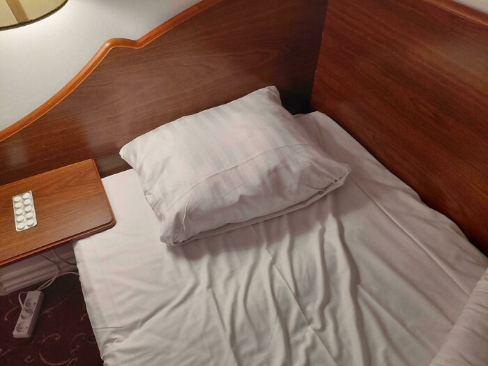 A single bed with a pillow and a nightstand, showing questionable home improvement due to its small size.