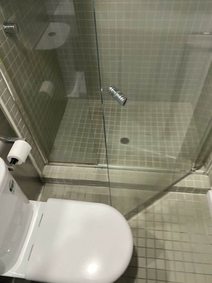 A shower stall with a toilet awkwardly placed right in front of the door, demonstrating questionable home improvement.