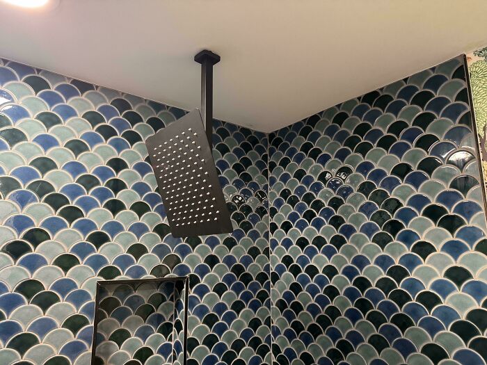 A modern home improvement shower with blue scalloped tiles and a black showerhead, demonstrating questionable results.