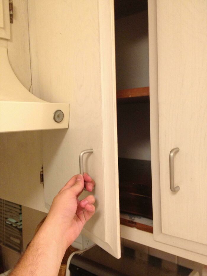 A hand awkwardly opening a home improvement cabinet that is too close to a wall, showing questionable results.