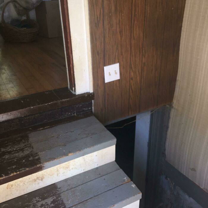 An interior doorway with wooden stairs leading down to a dark, unfinished space, showing questionable home improvement projects.