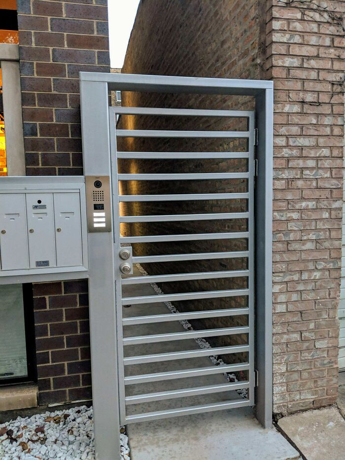 A modern silver gate between brick walls that is too narrow for entry, a questionable home improvement project.