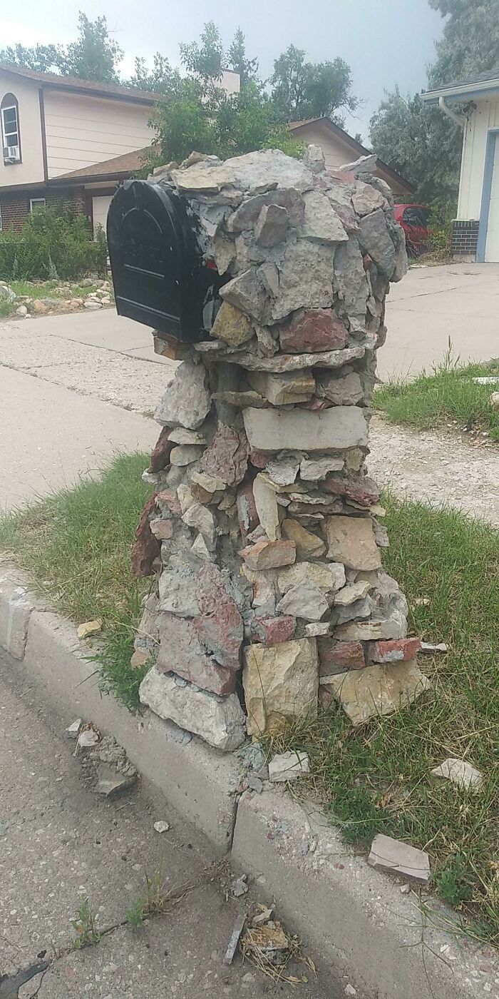 Questionable home improvement project of a mailbox post made from an unstable, haphazard pile of stones.
