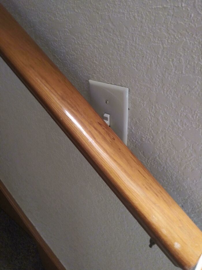 Questionable home improvement project showing a light switch awkwardly placed behind a wooden stair railing.