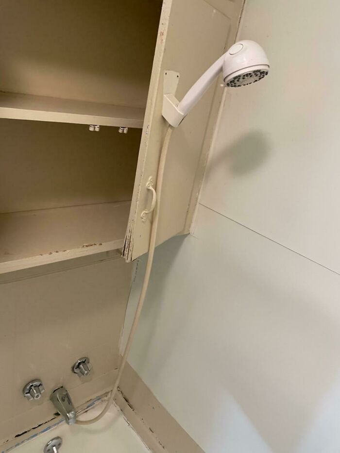 A shower head inexplicably mounted on the side of a wooden cabinet, highlighting questionable home improvement projects.