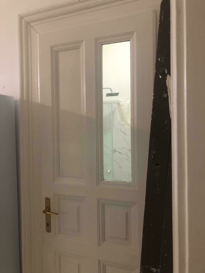 A white door with a clear glass panel revealing a bathroom shower, an example of questionable home improvement.