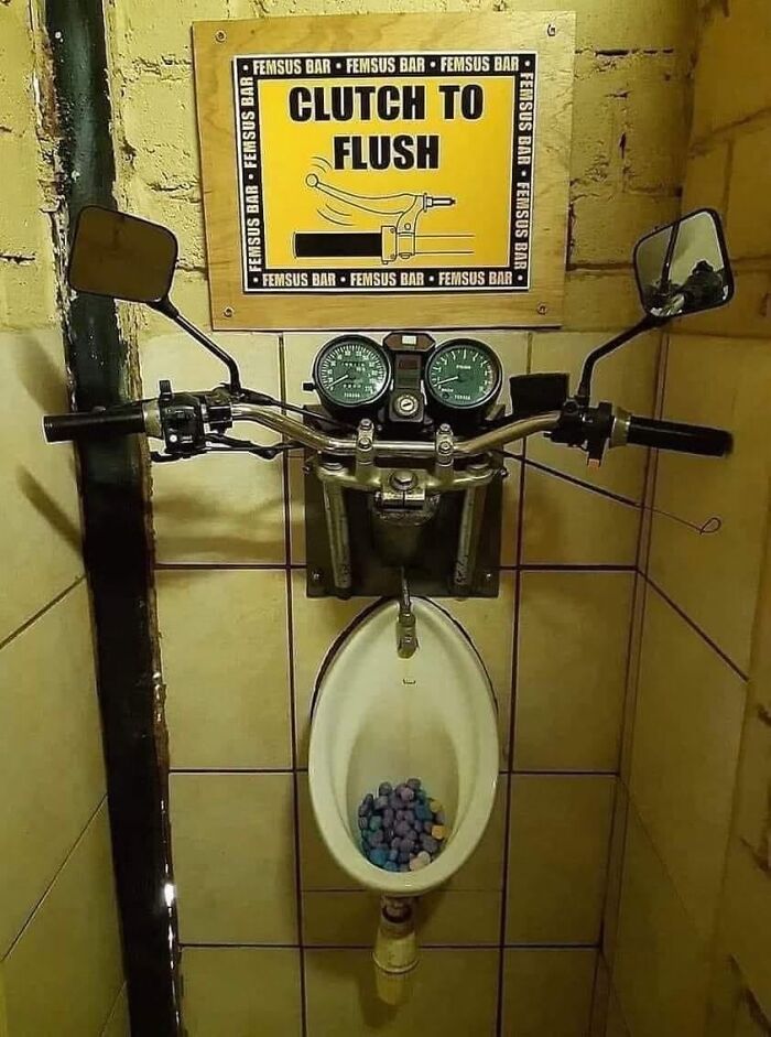 A restroom urinal with motorcycle handlebars and mirrors above it, showcasing questionable home improvement.