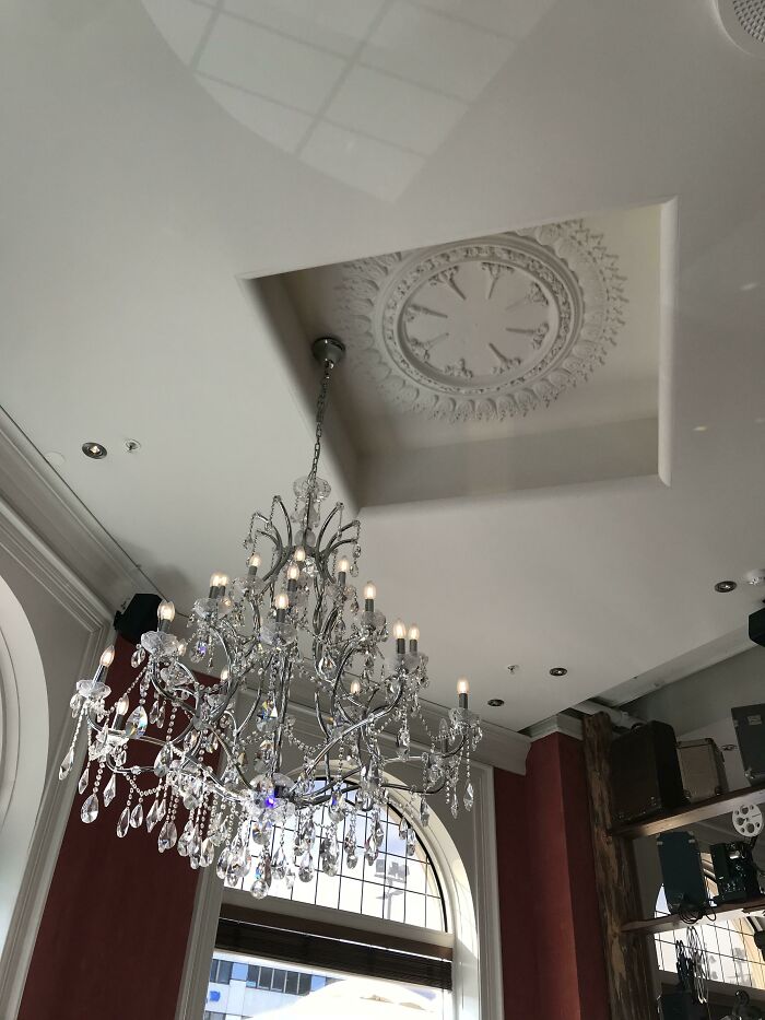 An ornate chandelier misaligned with a decorative ceiling medallion, showcasing questionable results from a home improvement project.