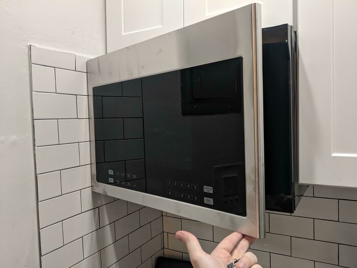 A microwave oven door obstructed by a wall, illustrating questionable results from home improvement projects.