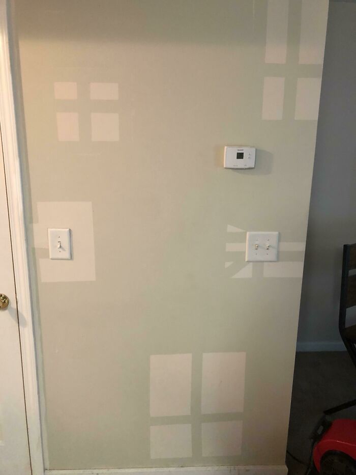 Questionable home improvement project: a beige wall with multiple light-colored rectangular patches, a thermostat, and light switches.