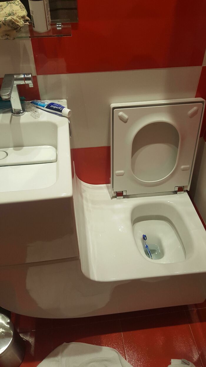 Questionable home improvement project: a toothbrush fallen into a toilet next to a sink with red and white striped tiles.