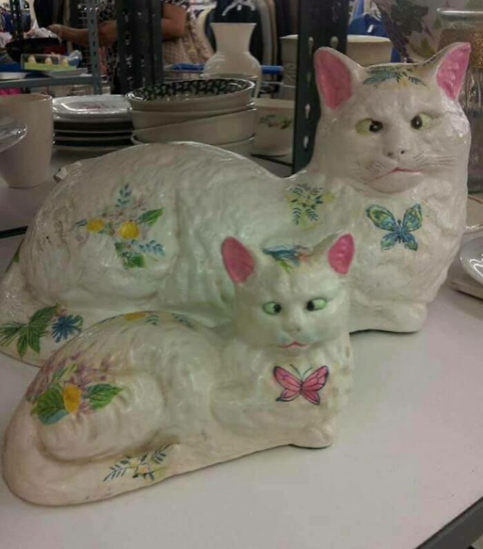 Two unhinged secondhand finds: ceramic cats with pink ears and floral and butterfly decorations.